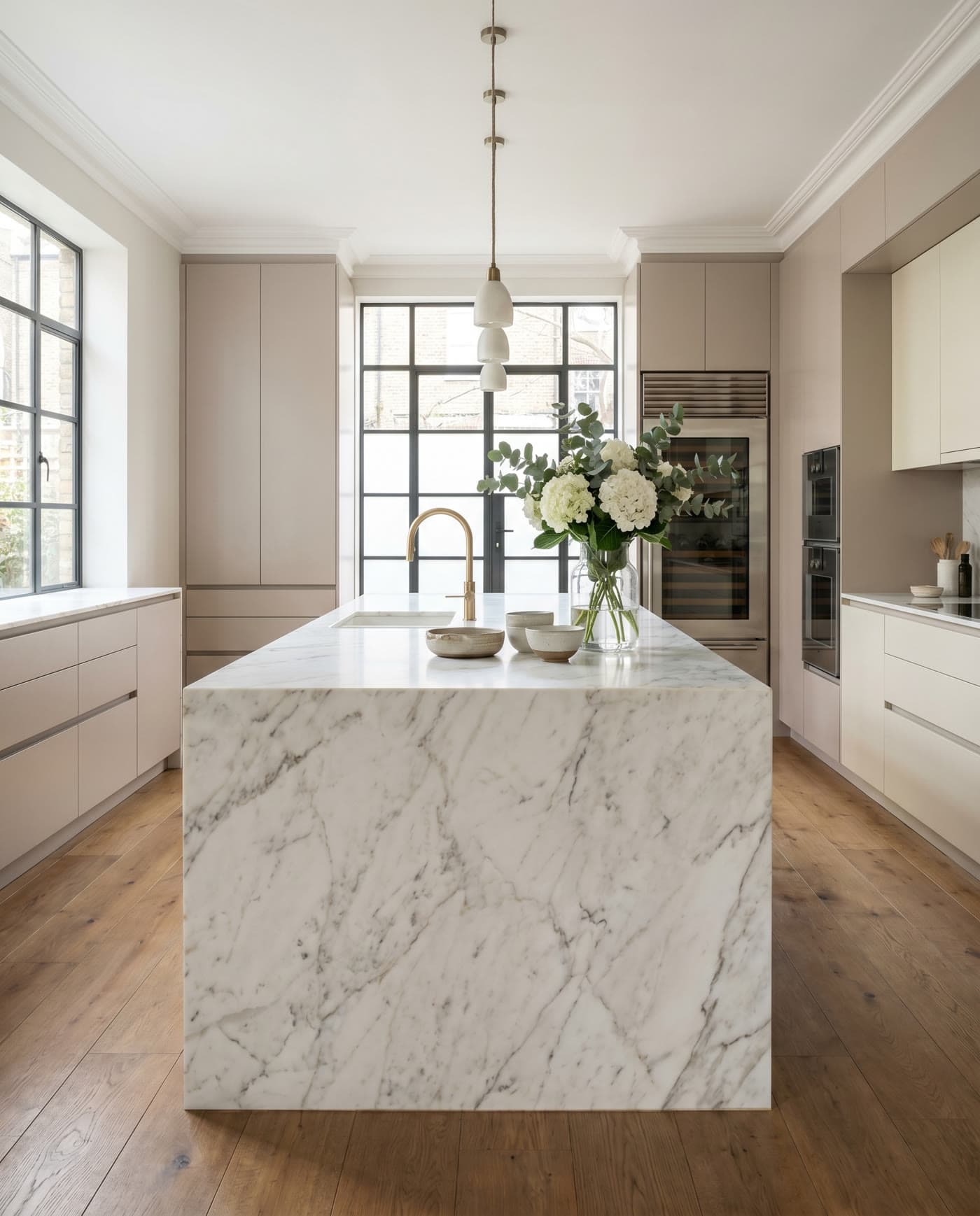 A renovated kitchen with a marble waterfall island and brass fittings